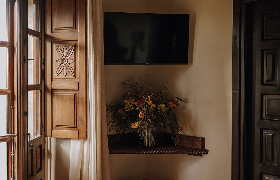 Detalle de jarrón con flores junto a la ventana de madera labrada